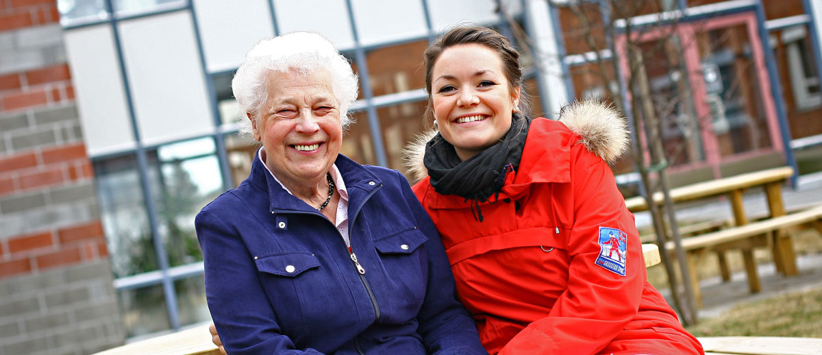 Eldre og yngre kvinne smilende på en benk
