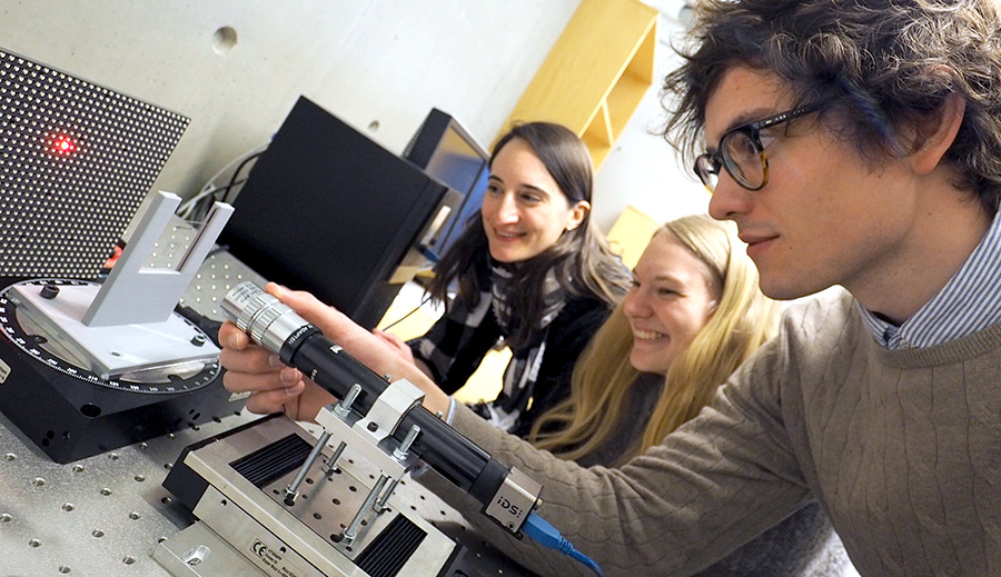 Tre studenter på fysikklaben som gjør et eksperiment med en laserstråle. Foto