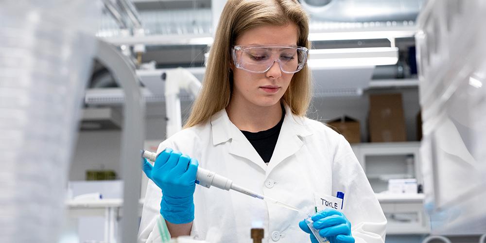 En masterstudent står på lab med en pipette i hånden. Foto. 
