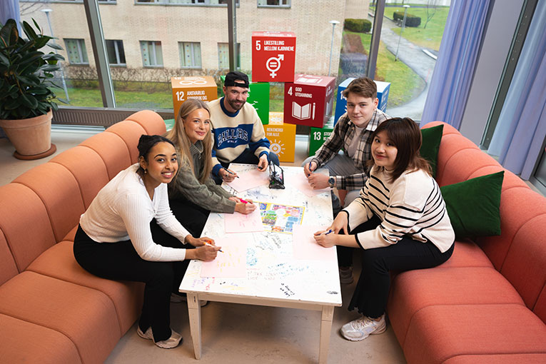 5 studenter, sitter i sofa og jobber rundt bord, på campus i Ålesund. Foto