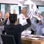 People around desk throwing papers in the air.