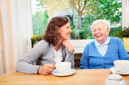 caregiver drinking coffee and talking with senior woman, having some fun - photo