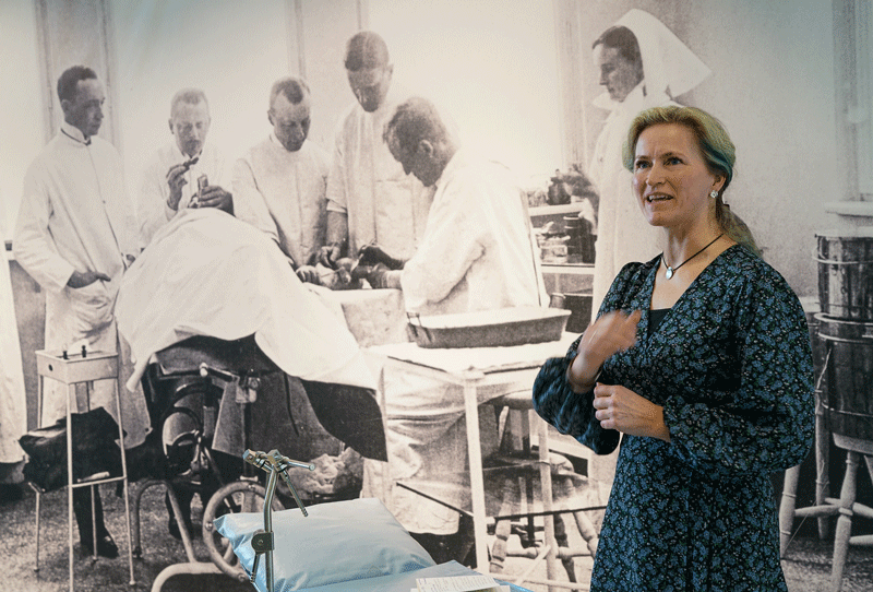 En person står foran et bilde i sorthvitt og prater. På bildet er det leger og sykepleiere fra 1900-tallet som utfører en operasjon.