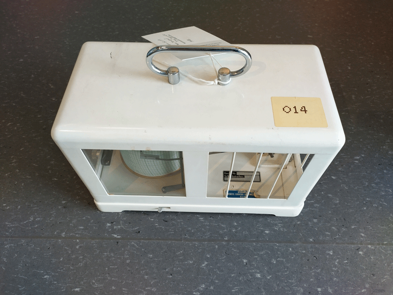 Hvit rektangulær boks i metall, med åpninger på sidene og håndtak på toppen. Sett ovenfra.