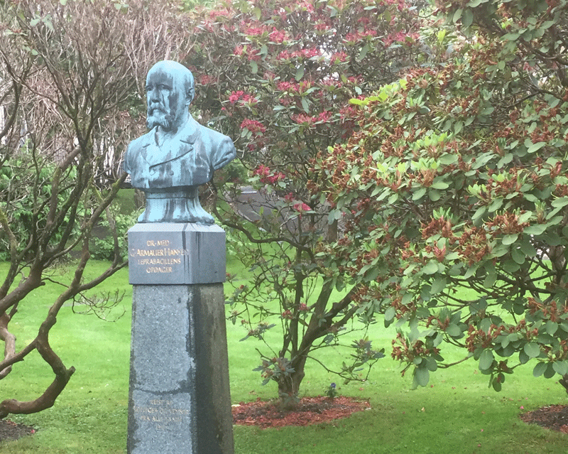 statue med byste av en person, i en park med trær og gress.