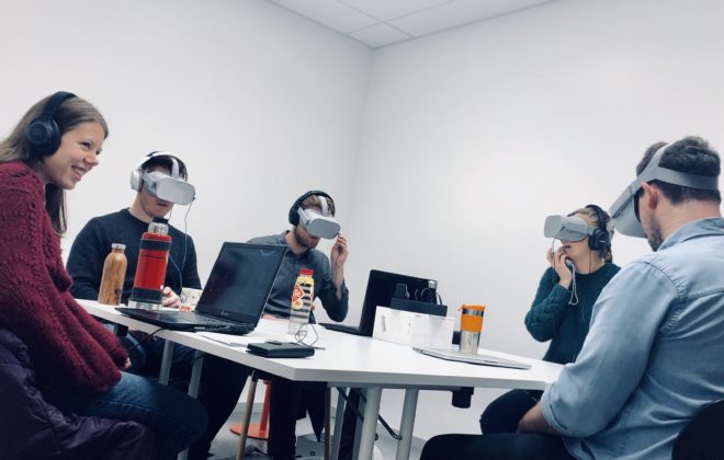 5 studenter sitter rundt et bord, fire av dem har på VR-briller. Foto.