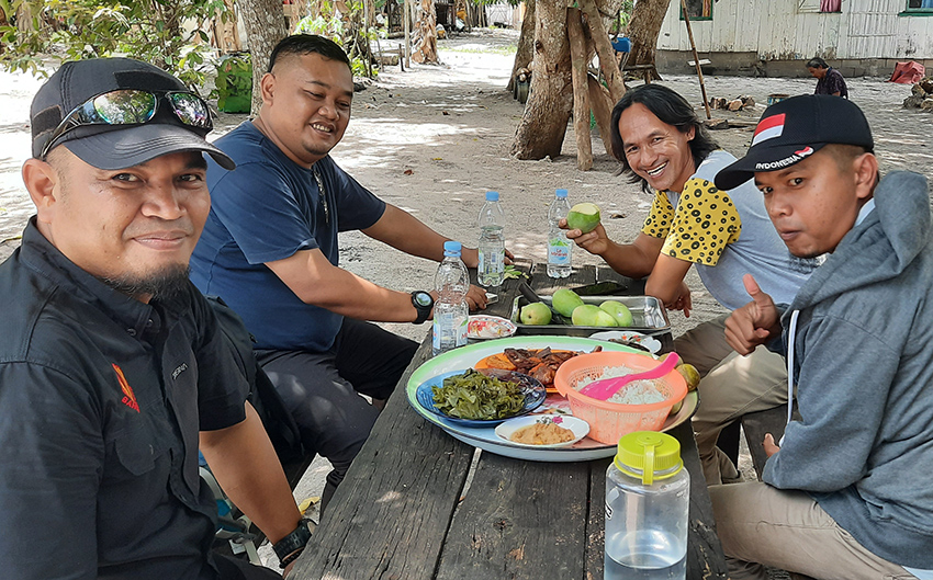 Four smiling men sharing a meal outdoors. Photo. 