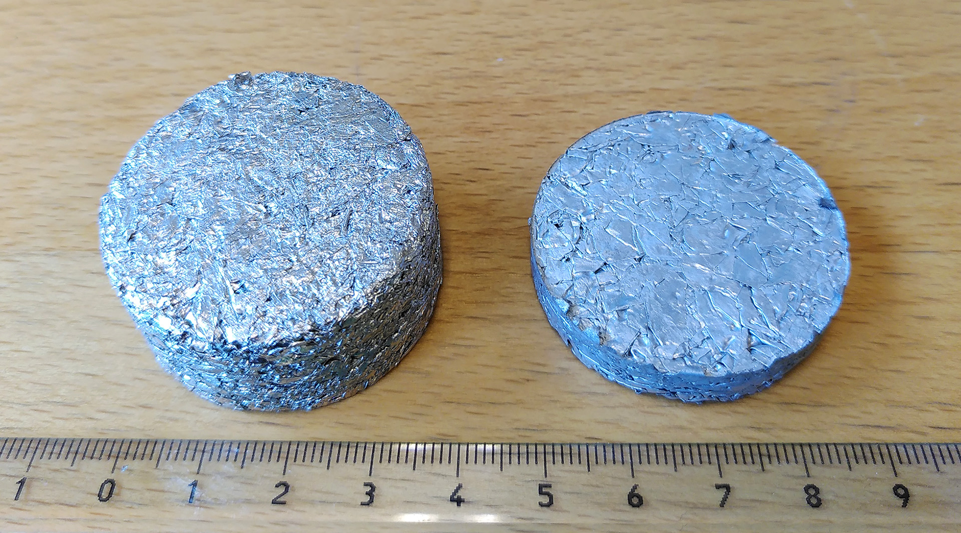 Aluminium foils compacted into 2 briquettes with a ruler next to them. Photo