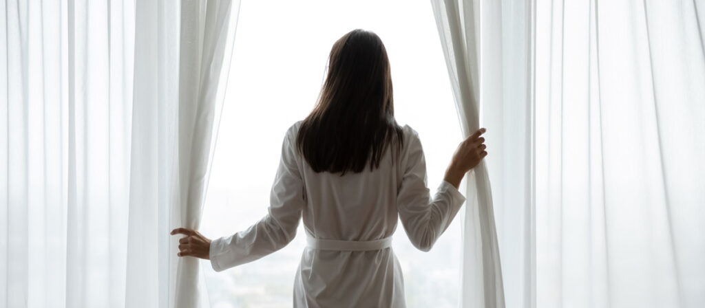 woman opening curtains on hotel room, admiring the view. photo