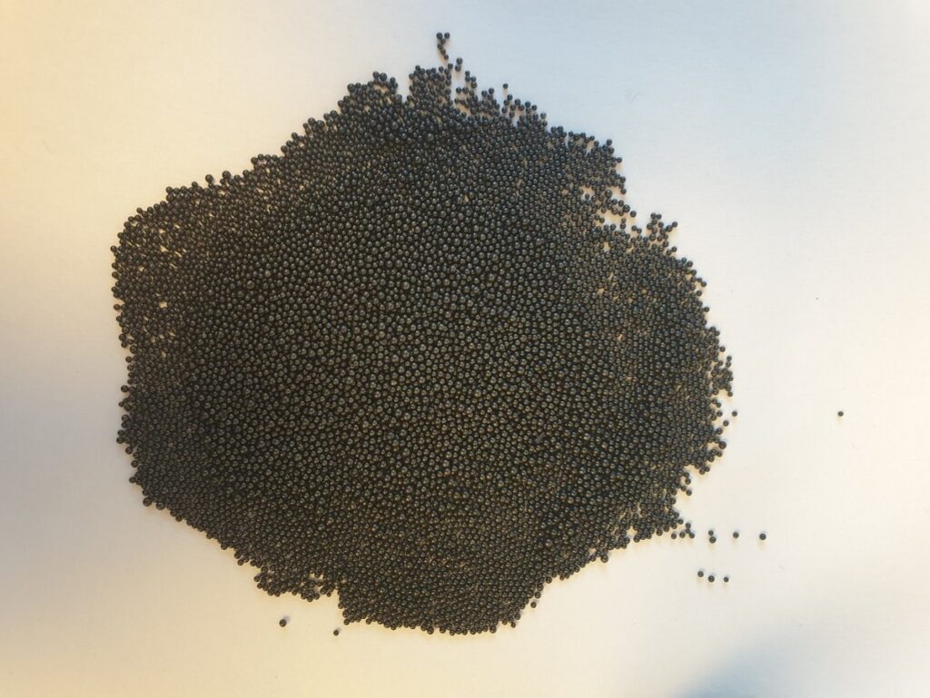Several thousand black, shiny beads in a pile on a white surface.