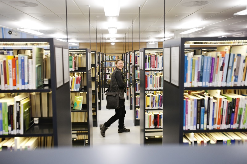 Woman walking along book shelves in the library