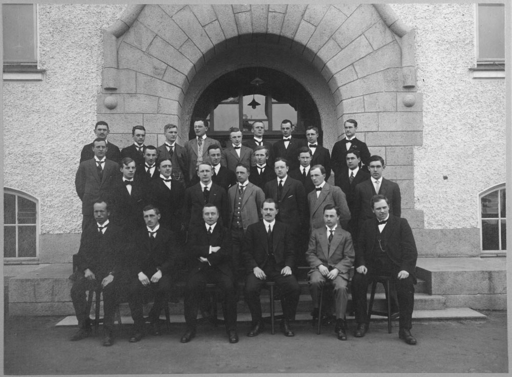 Men in suits posing outside a concrete building