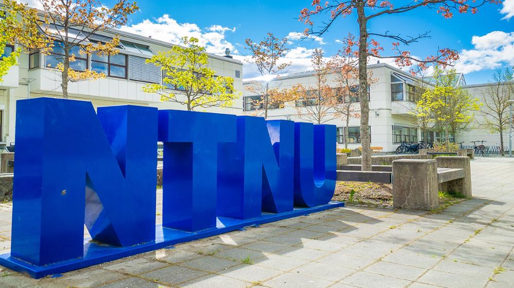 NTNU i store blå bokstaver plassert utendørs