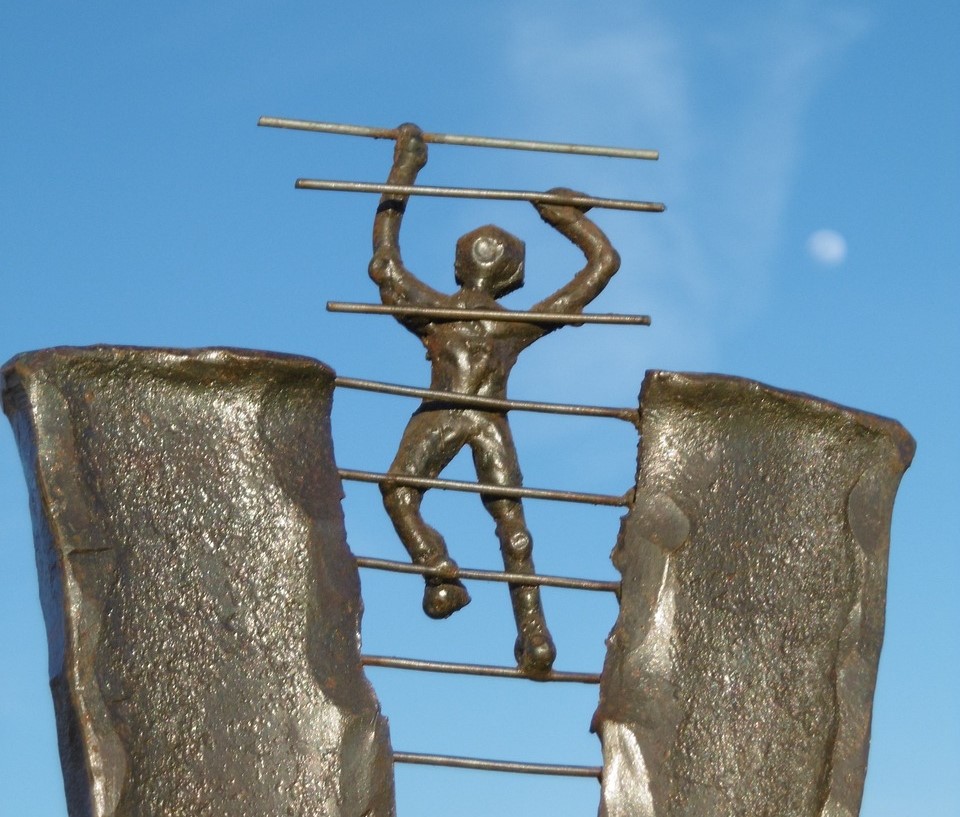 Foto av statue av en person som klatrer på en stige.