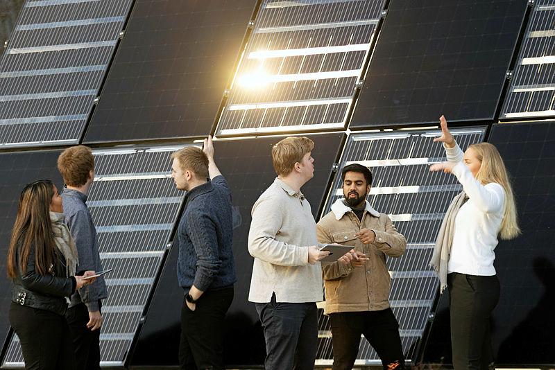 En gruppe mennesker står foran en bygning med solcellepanel på veggene.