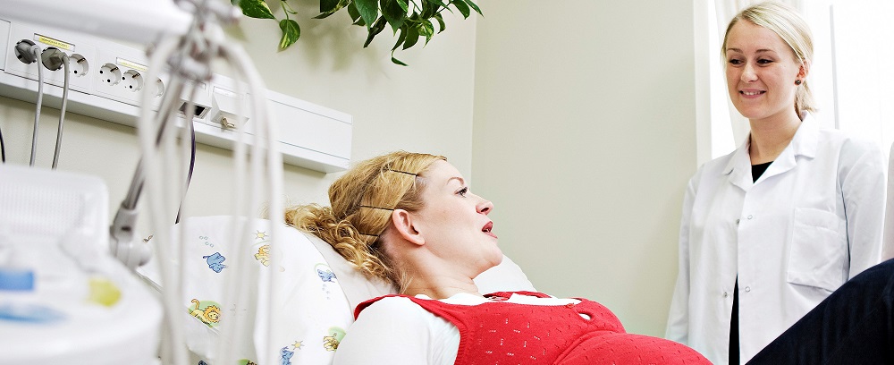 Gravid kvinne i sykehusseng som snakker med en sykehusansatt i hvit frakk