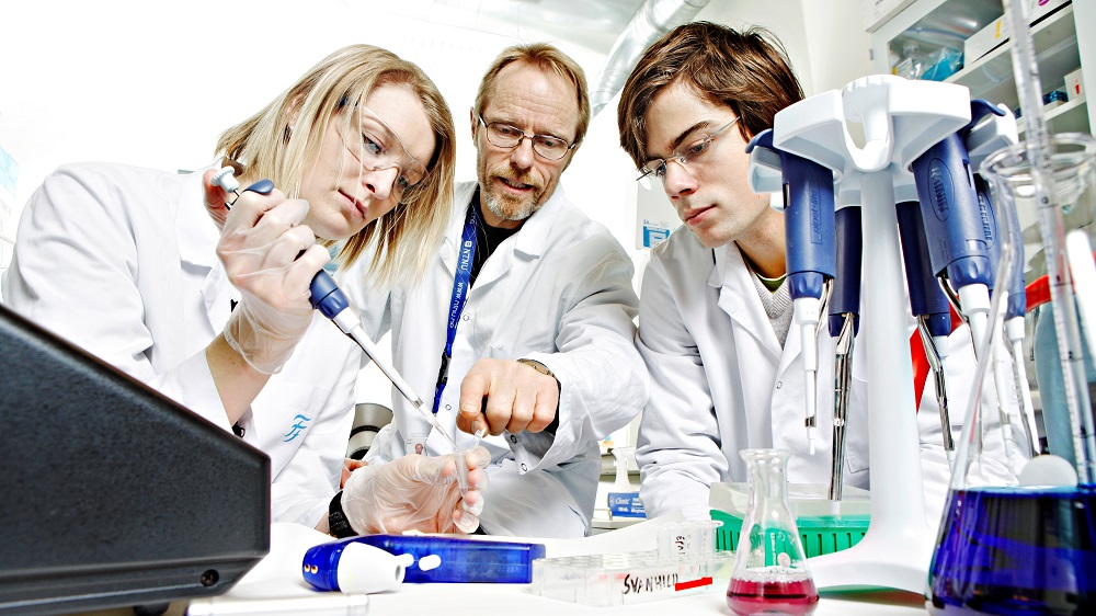 Tre personer arbeider med pipette i laboratoriet