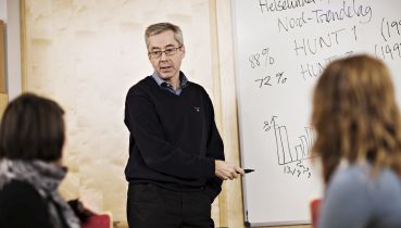 En professor peker på tavla mens to personer hører på