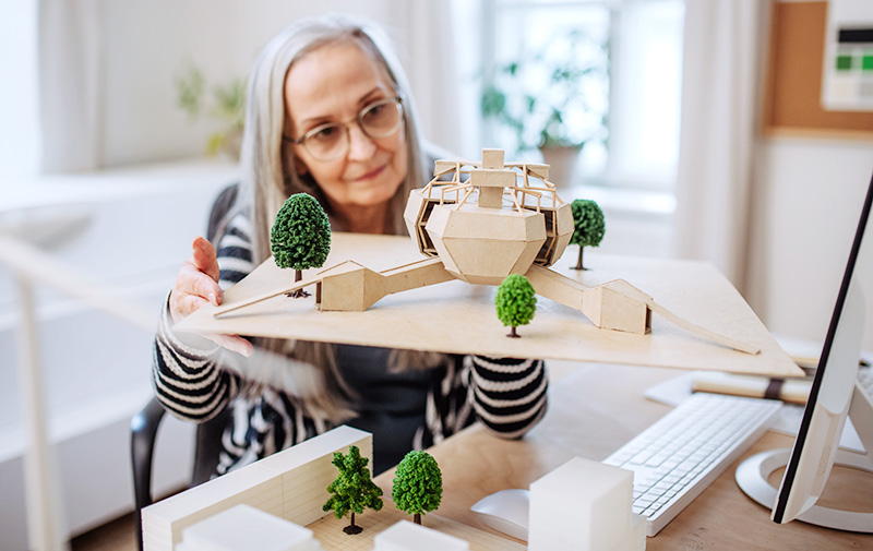 Ei eldre kvinne som ser på en modell av bygninger med trær. Foto