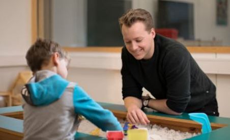 Foto av psykologistudent som leker med en gutt i klinikklokalet til Institutt for psykologi