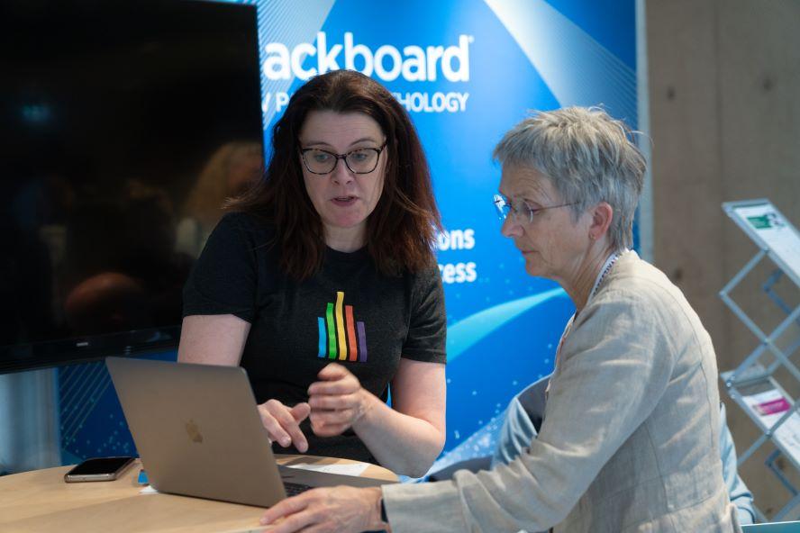 Foto av en stand for Blackboard. En kvinne viser en annen kvinne noe på en dataskjerm.