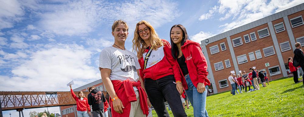 tre studenter står ute på campus og smiler. foto