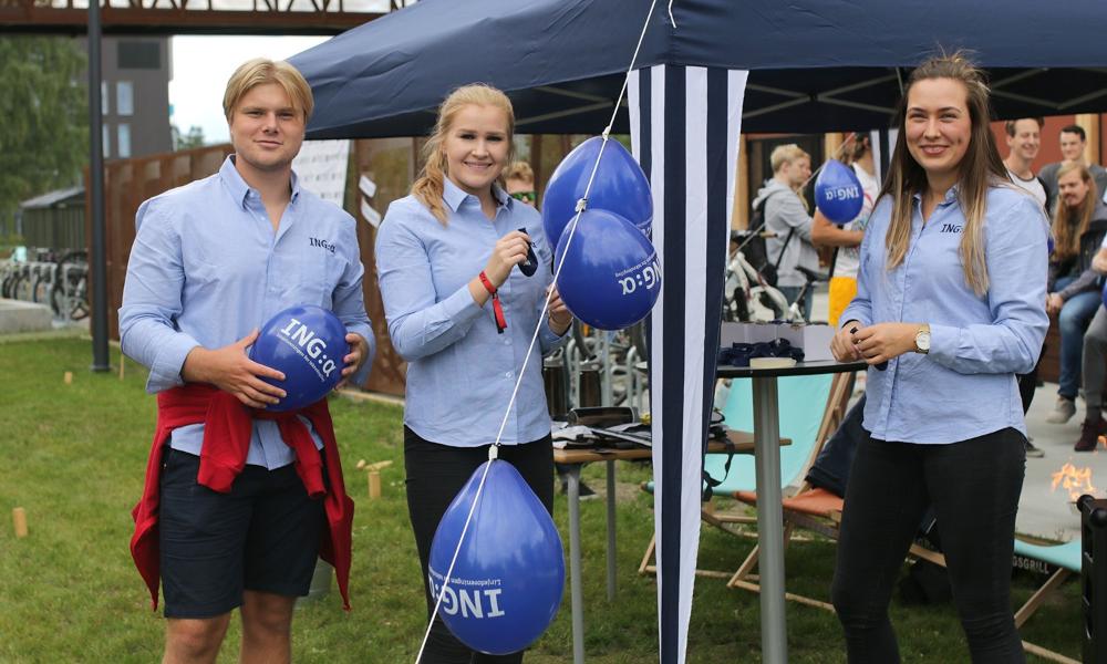 Tre studenter henger opp ballonger og smiler. Foto