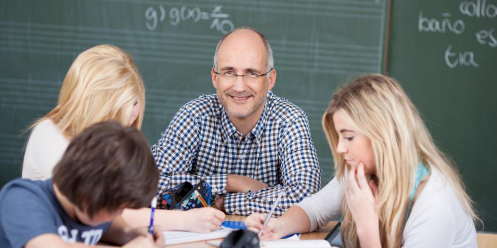 Mannlig mattelærer sitter ved et gruppebord med elever.