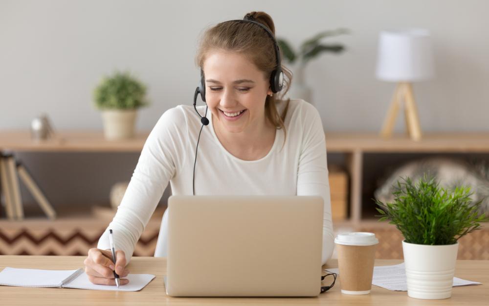 Smilende kvinne som prater i headset mot oppslått laptop. 