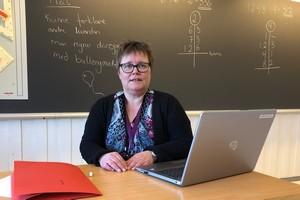 Kvinnelig lærer med pc sittende i klasserom foran tavle