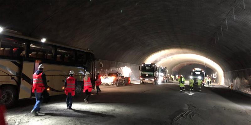 Tunnel med flere kjøretøy og personer i arbeidstøy med refleks.  