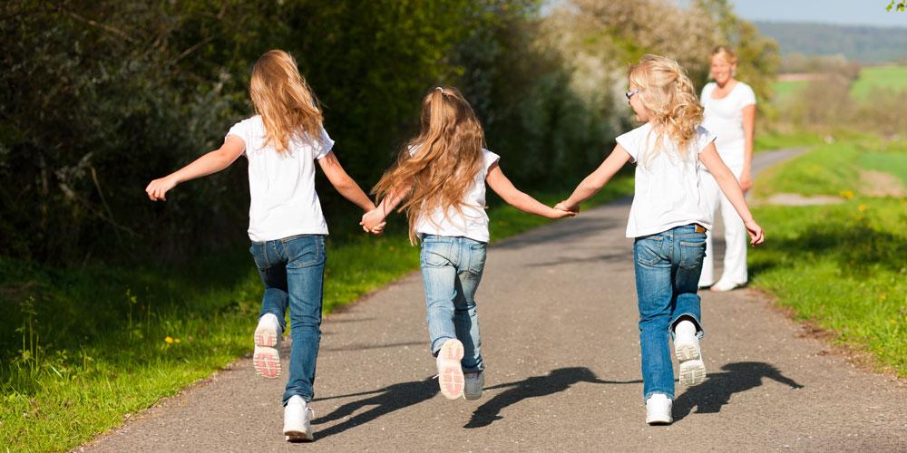 Tre jenter løper hånd i hånd på en gangvei.