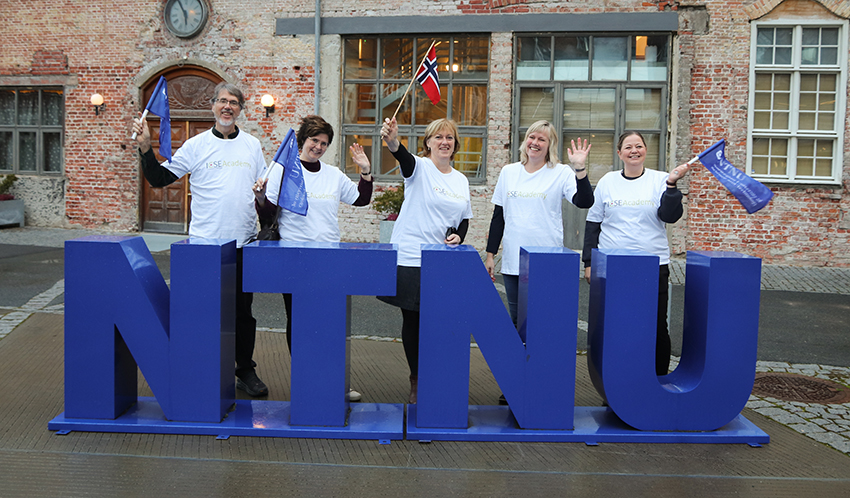 5 ICSE-forskere står bak NTNU-bokstaver med like ICSE t-skjorter og flagg. Foto