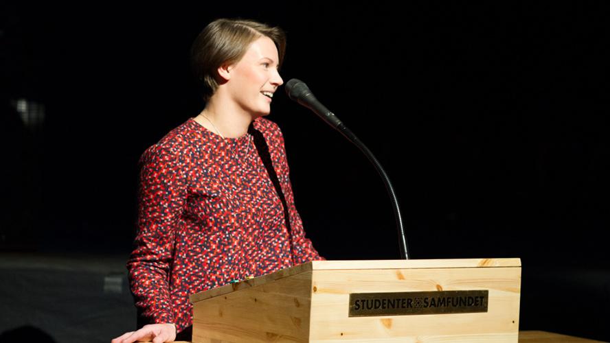 Bilde av kvinne som står ved talerstol og snakker i mikrofon.