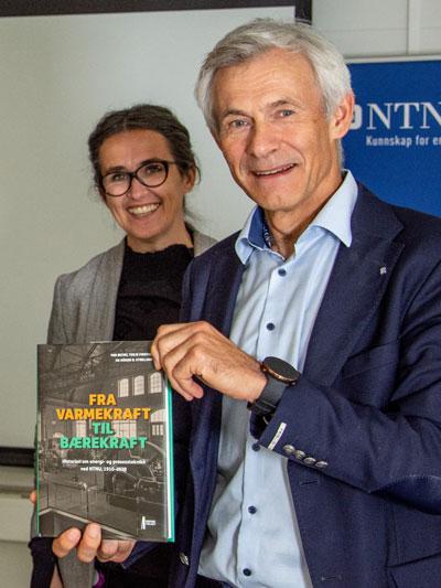 Olav Bolland holder opp en bok med oransje og grønn tittel. Terese Løvås smiler i bakgrunnen. Foto