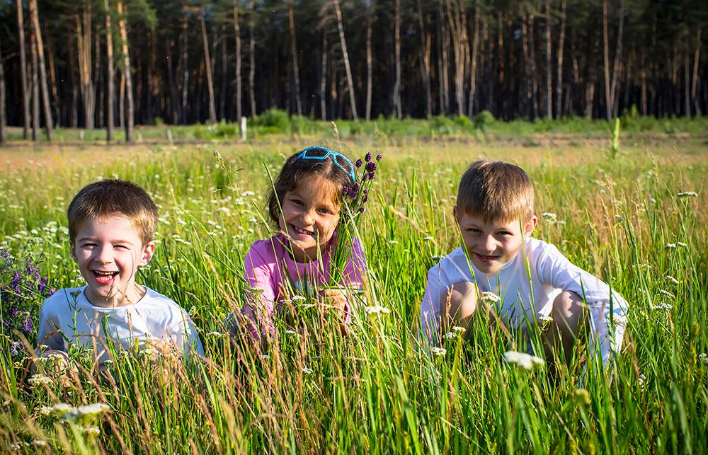 Tre unge smilende barn i blomstereng