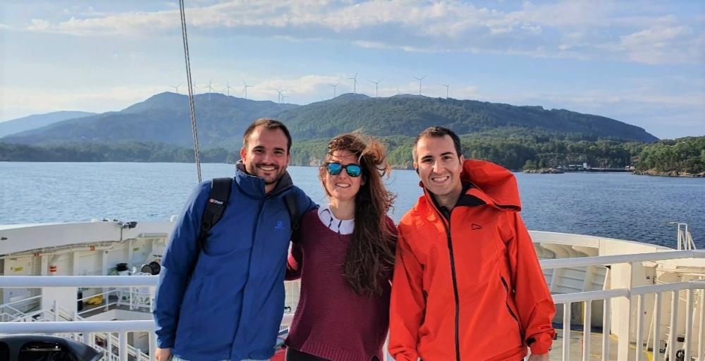 Tre PhD-studenter på ei ferge med vindmøllepark i bakgrunnen