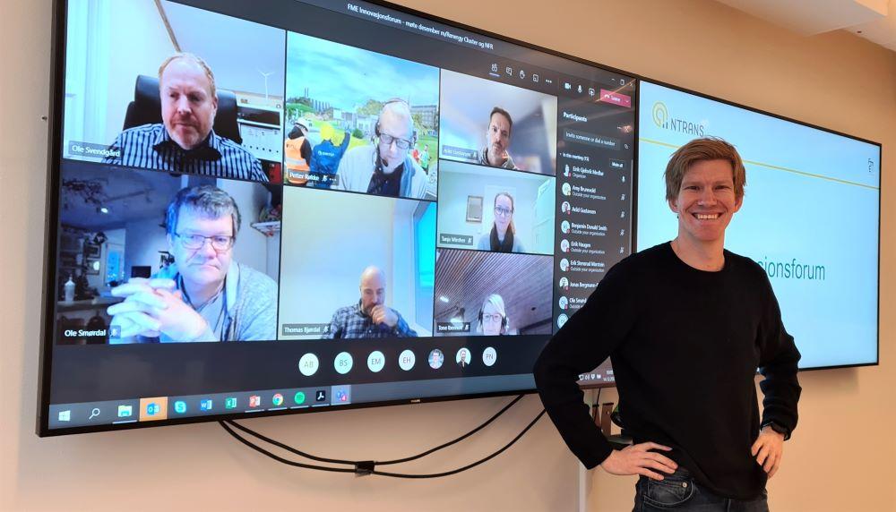 Eirik Medbø foran storskjermer med bilder av forumdeltakere