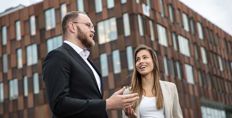 Mann og kvinne prater sammen foran stor bygning