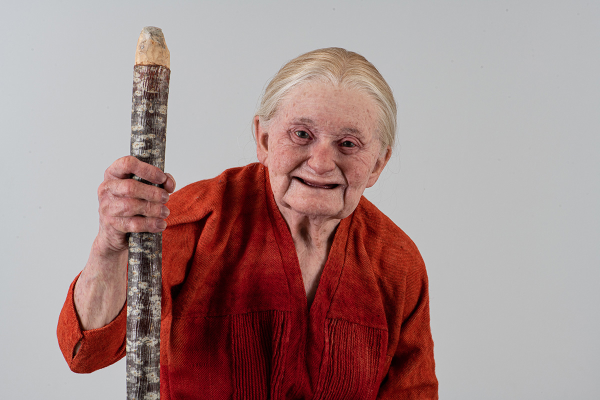 Modell av smilende gammel kvinne med hvitt hår. Foto.