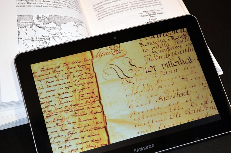 Åpen bok og et digitalt lesebrett som viser en håndskreven kilde. Foto