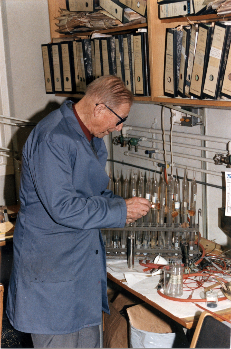 Prof. em. i teknisk elektrokjemi Jomar Brun (1904-1993) på sitt kontor. Foto: Ukjent/NTNU UB: Mann med kjemiglass står ved en seksjon.