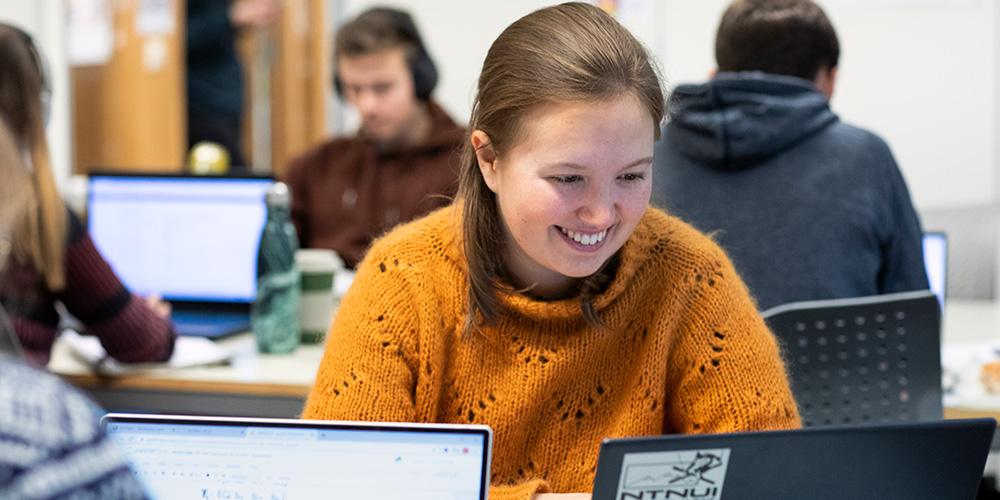 En kvinnelig student smiler under arbeid i lesesal. Foto