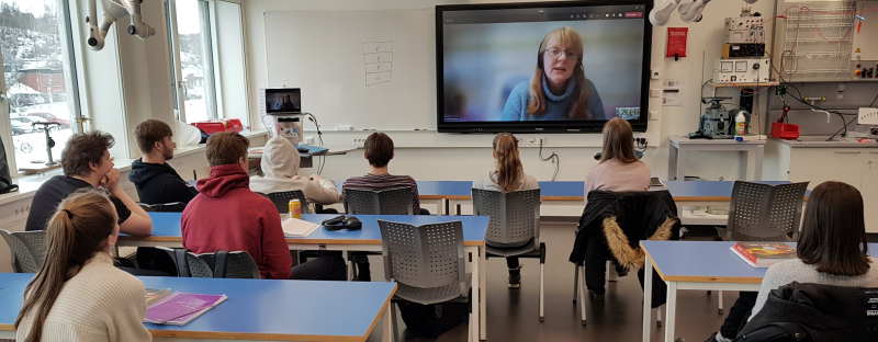 Elever i et klasserom som ser på en person på storskjerm. Foto.
