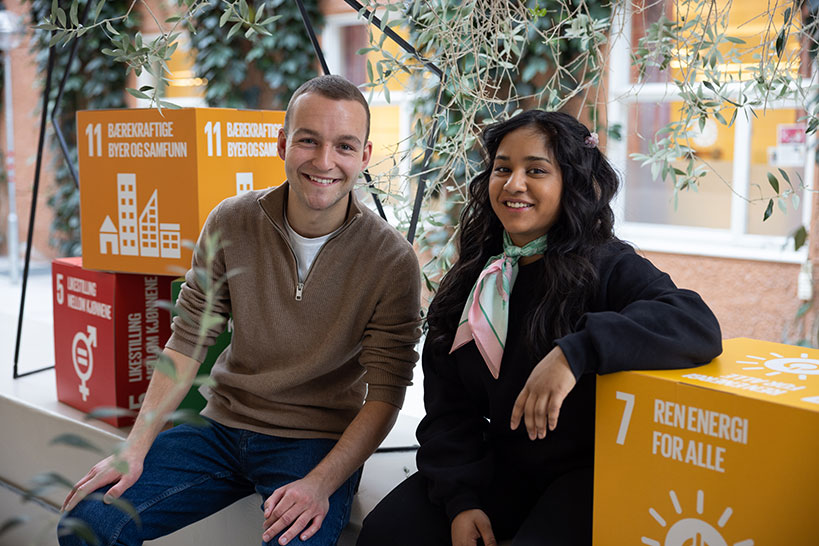 2 glade studenter, med bokser av bærekraftmålene, på campus i Trondheim. Foto
