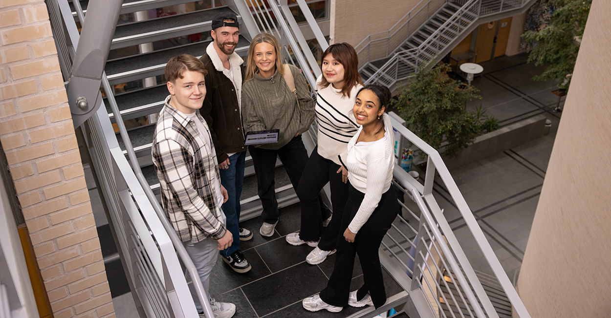Fem studenter står i en trapp og smiler mot kamera